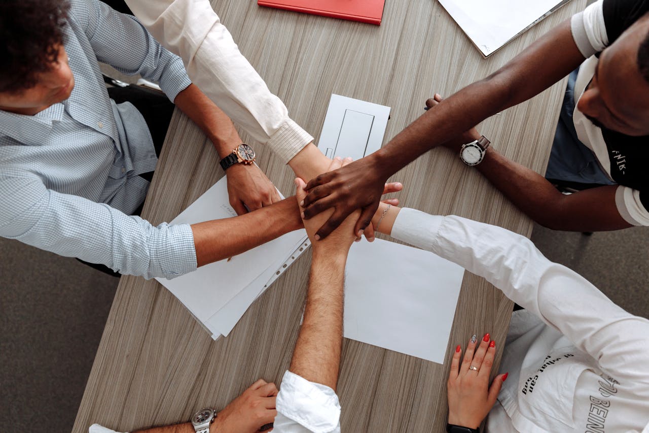 Diverse photo image of five extended arms with hands on top of each other symbollizing collaboration or like a sports team