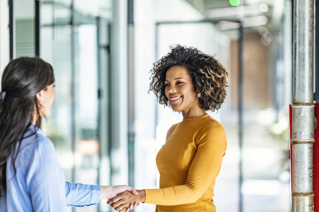 Photo image of two diverse business women shaking hands and smiling in a modern business office setting